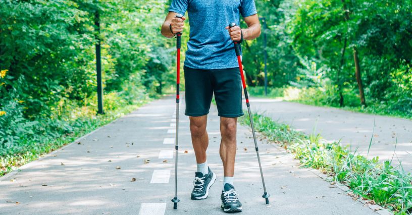 Mężczyzna maszeruje z kijkami do nordic walking po asfaltowej ścieżce wśród drzew