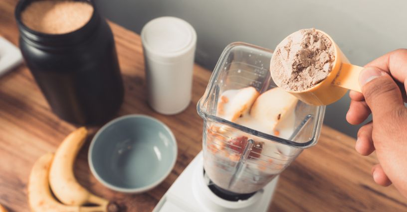 Sportowiec dorzuca miarkę odżywki białkowej do miksera, aby zrobić shake proteinowy