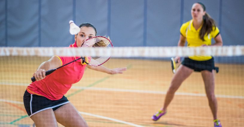 Kobieta w stroju sportowym odpija lotkę rakietą do badmintona podczas meczu na hali