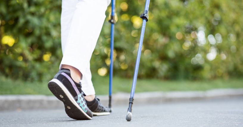 Gumowe buciki w kijkach do nordic walking trzymanych przez kobietę maszerującą po parkowej alejce