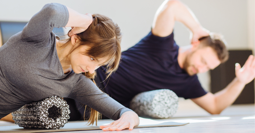 Dwoje ludzi ćwiczy na matach fitness, używając wałków do masażu