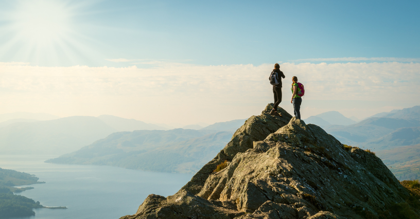 Dwoje turystów w sportowej odzieży podziwia panoramiczny widok ze skalistego szczytu