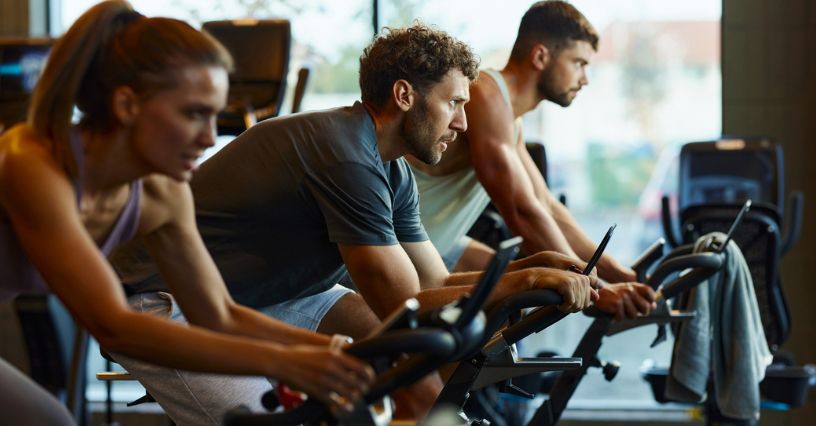 Trzy osoby jadą na rowerach spinningowych podczas zajęć indoor cycling