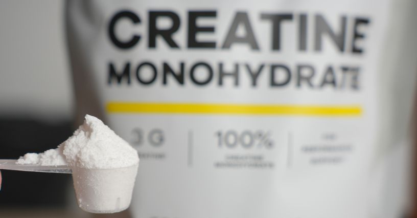 Miarka z dawką kreatyny na tle paczki z monohydratem kreatyny