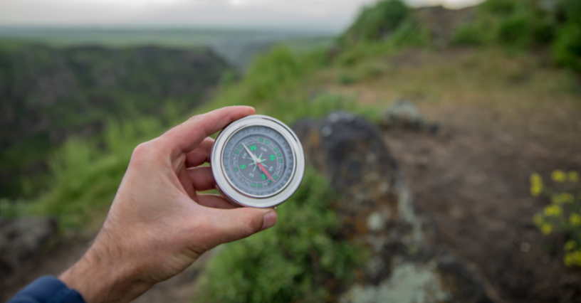 Osoba trzyma kompas podczas wędrówki po zielonych wzgórzach
