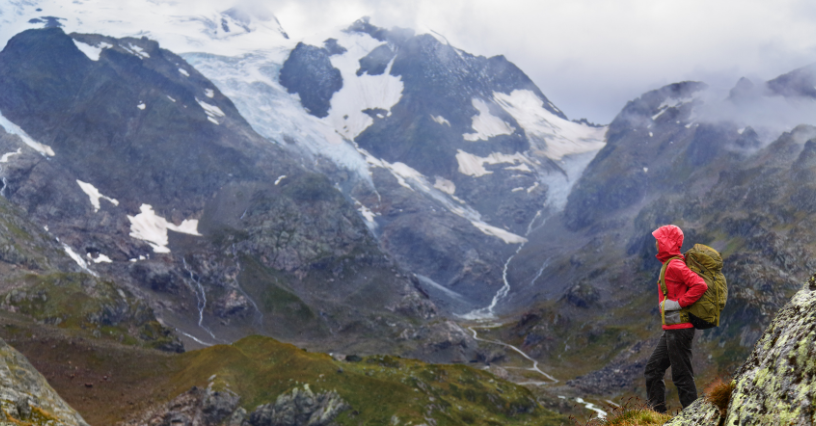 Kobieta w kurtce z membraną i z plecakiem podziwia majestatyczne górskie krajobrazy