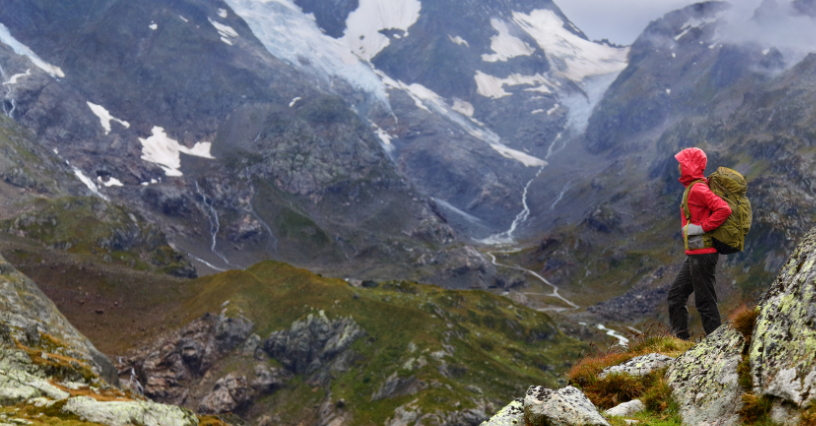 Osoba w turystycznej kurtce przeciwdeszczowej stoi na skale, podziwiając górski krajobraz