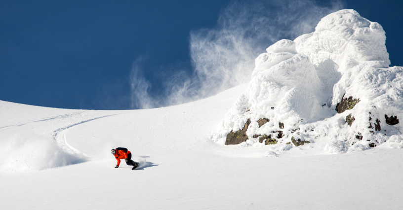 Snowboardzista w czerwonej kurtce zjeżdża po dziewiczym, zaśnieżonym stoku