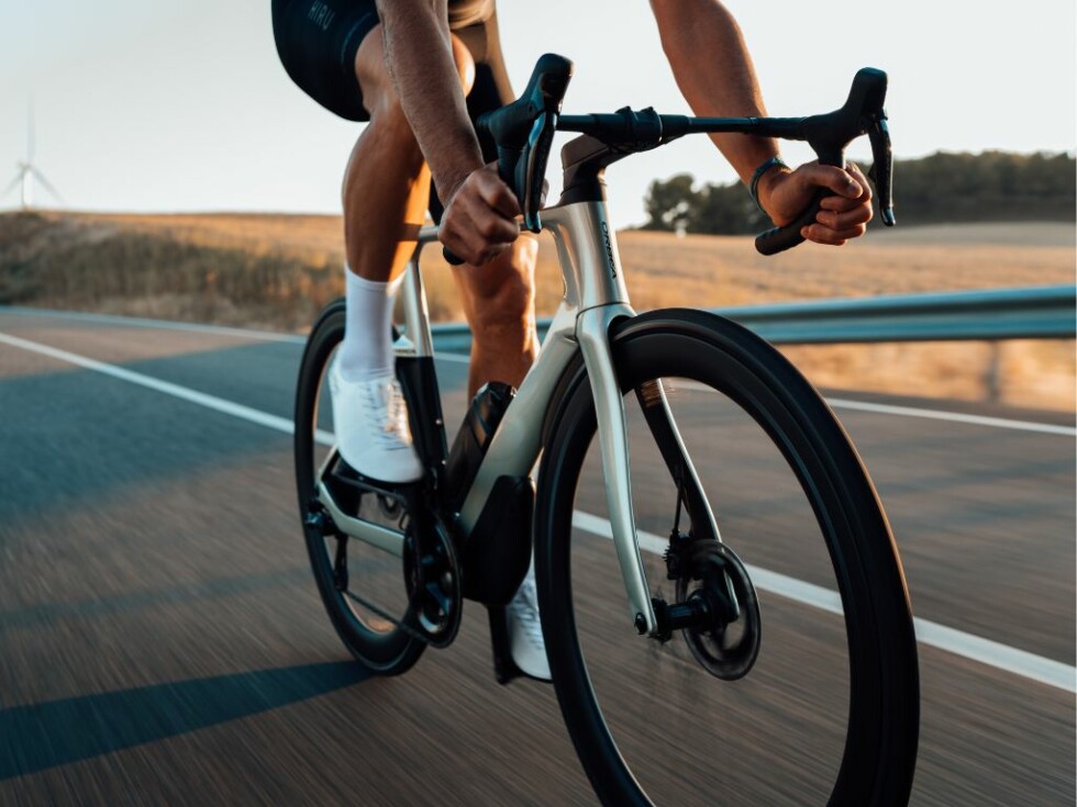 Kolarz na rowerze Orbea jedzie po otwartej drodze, korzystając z letniej pogody