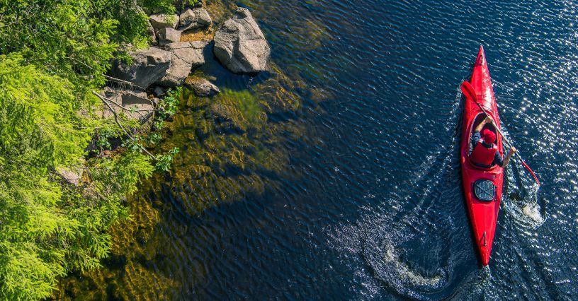 Mężczyzna w kamizelce asekuracyjnej płynący w kajaku po spokojnej rzece