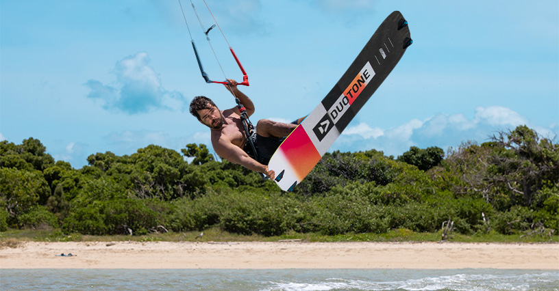 Mężczyzna trzymający się bara w skoku nad wodą na desce do kitesurfingu