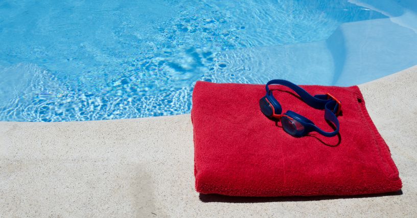 Ręcznik szybkoschnący i okulary pływackie położone na brzegu basenu