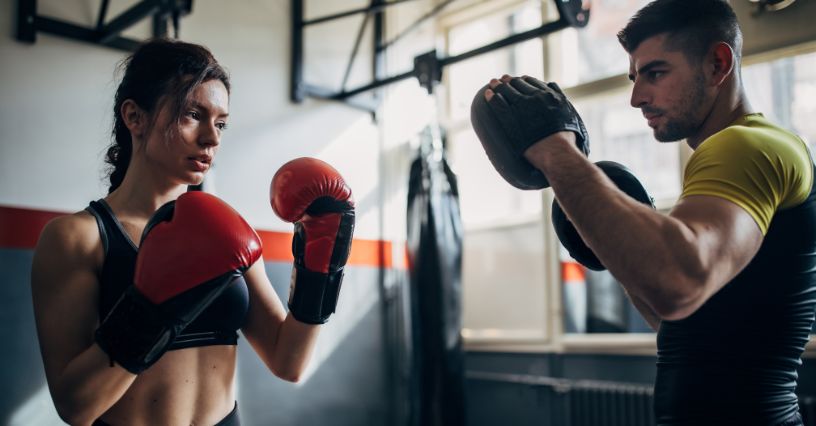 Kobieta w rękawicach do boksu trenująca uderzenia z trenerem