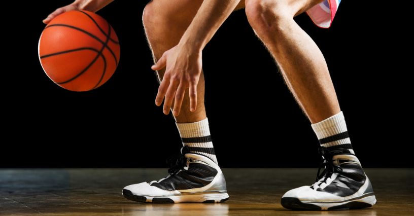 Koszykarz w butach koszykarskich z wysoką cholewką kozłuje piłkę na boisku w hali sportowej