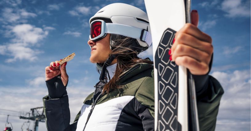 Narciarska jedząca przekąskę w przerwie od jazdy na nartach po stoku