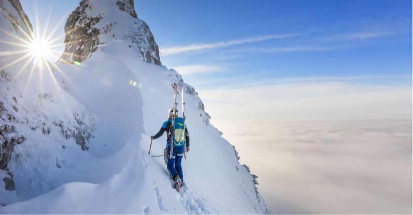 Turystka w czasie zimowej wyprawy górskiej z plecakiem lawinowym i przypiętymi do niego nartami