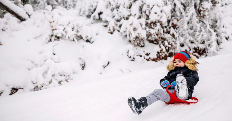 Chłopczyk w zimowej odzieży zjeżdżający na ślizgaczu typu jabłko po śniegu