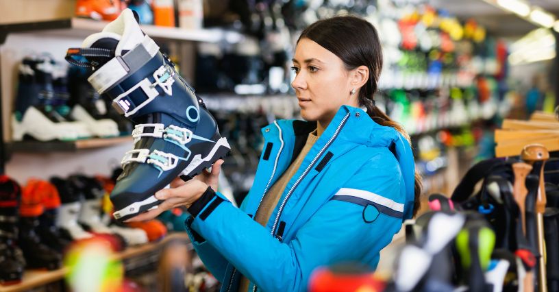 Kobieta wybiera buty narciarskie w sklepie sportowym