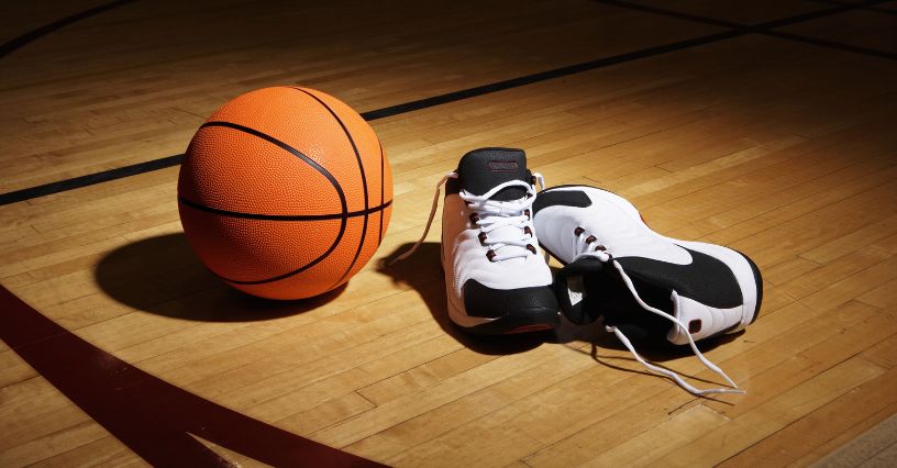 Biało-czarne buty do koszykówki ze średnią cholewką leżące na parkiecie obok piłki do kosza