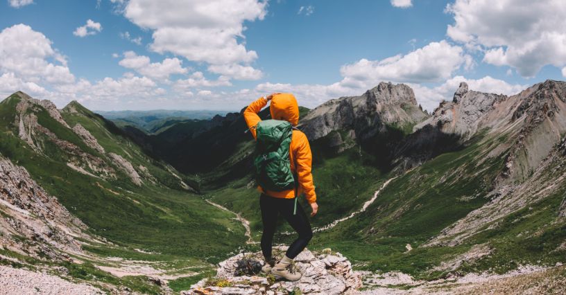 Mężczyzna w kurtce i plecaku trekkingowym podziwiający górską dolinę