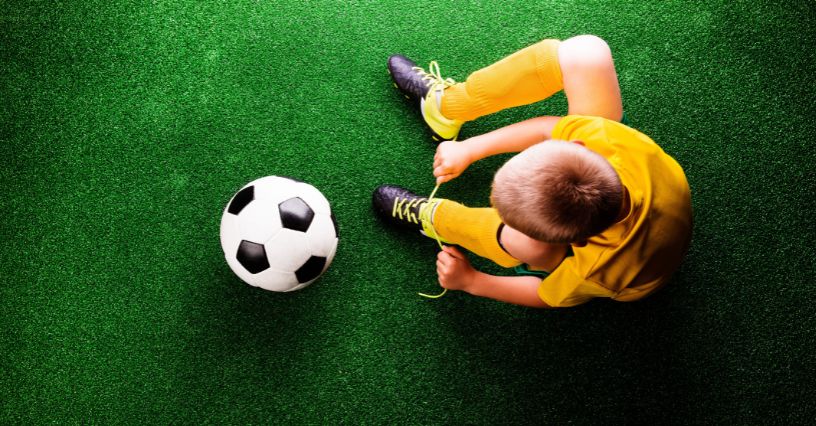 Chłopiec stroju piłkarskim zawiązuje turfy siedząc na sztucznej murawie