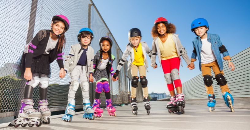 Grupa dzieci na rolkach stojąca w kaskach i ochraniaczach na łokcie i kolana