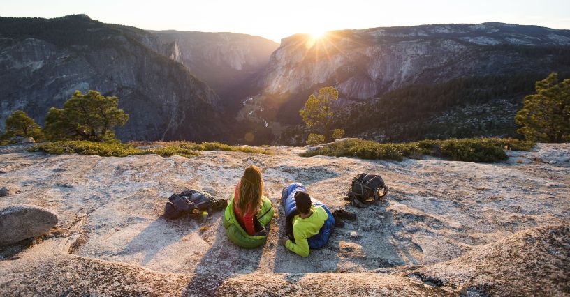 Para leżąca w śpiworach turystycznych i obserwująca zachód słońca w górach
