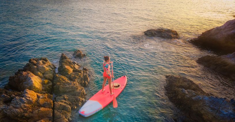 Kobieta pływająca na desce SUP między skałami o zachodzie słońca