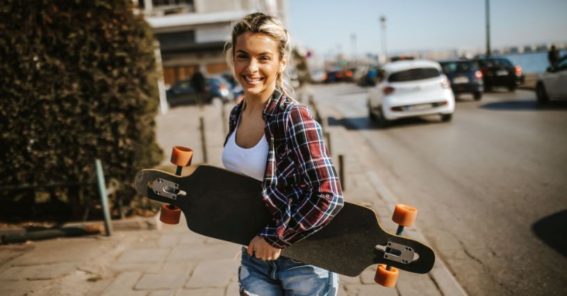 Kobieta trzymająca czarny longboard stojąca na miejskim chodniku