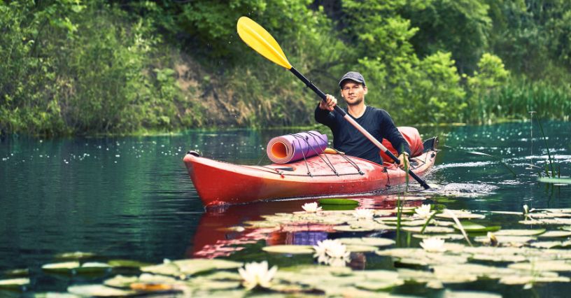 Mężczyzna pływający samodzielnie kajakiem po rzece pełnej lilii wodnych