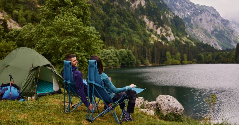 Para siedząca na krzesłach turystycznych przy namiocie nad jeziorem