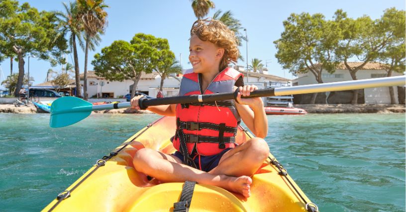 Chłopiec w kamizelce ratunkowej pływający kajakiem niedaleko domów