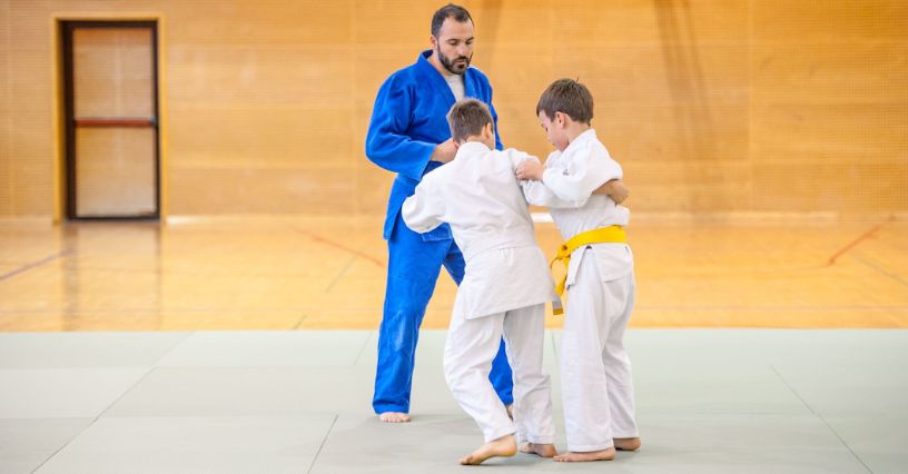 Chłopcy trenujący wytrącenia w judo pod okiem trenera