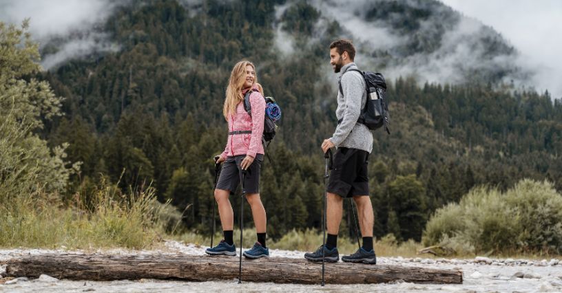 Para turystów z plecakami i kijkami idąca po kłodzie drewna