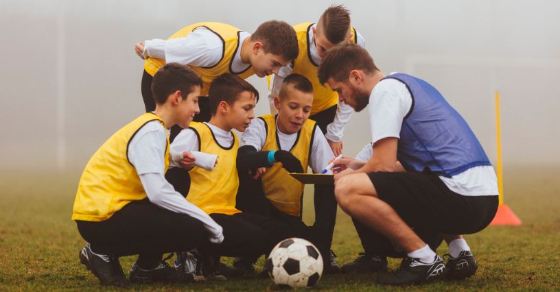 Trener objaśniający młodym piłkarzom ćwiczenia w trakcie treningu