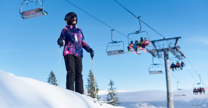 Kobieta w stroju narciarskim na tle wyciągu narciarskiego