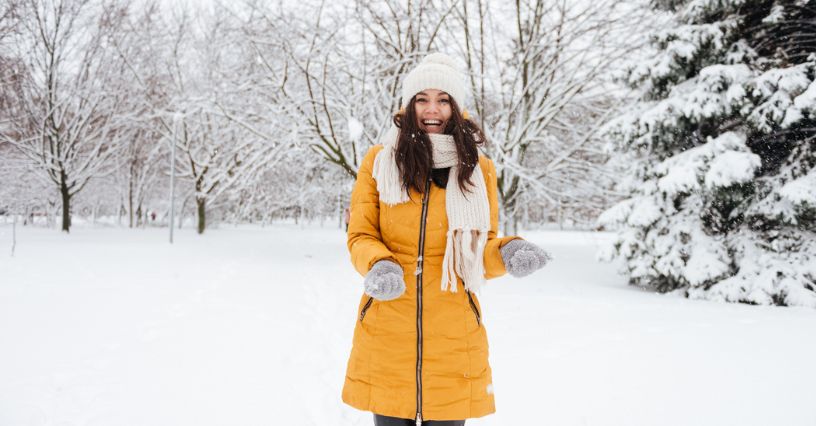 Uśmiechnięta kobieta w żółtym płaszczu stojąca w parku na śniegu