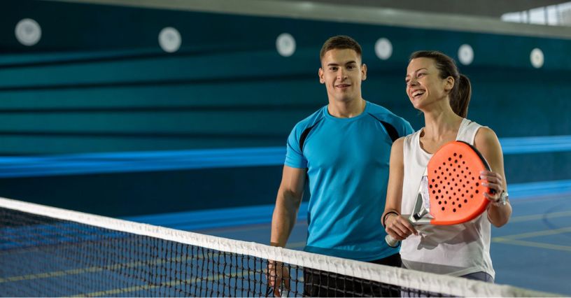 Uśmiechnięta kobieta z rakietą i mężczyzna stojący na boisku do padla