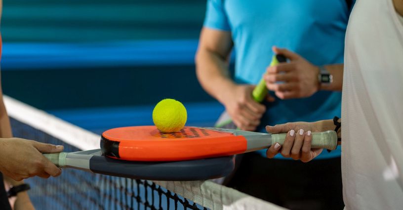 Rakiety do padla z piłką ułożone na sobie nad siatką do gry