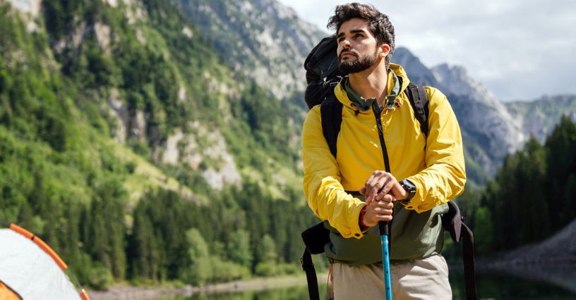 Mężczyzna w kurtce przeciwdeszczowej podpierający się na kijku trekkingowym i podziwiający górskie widoki