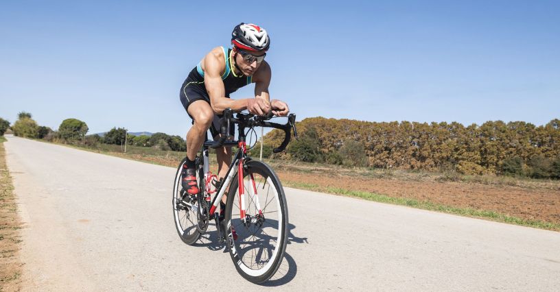 Kolarz w profesjonalnej odzieży rowerowej i kasku jadący na rowerze w aerodynamicznej pozycji