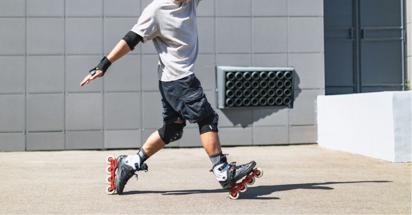 Mężczyzna w ochraniaczach na kolanach i łokciach jeździ na rolkach na tle betonowej ściany