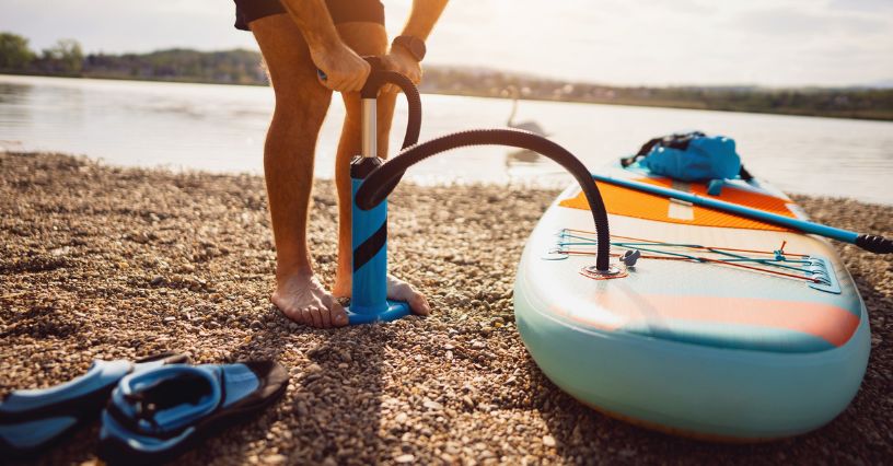 Mężczyzna używa pompki ręcznej do napompowania deski SUP na plaży