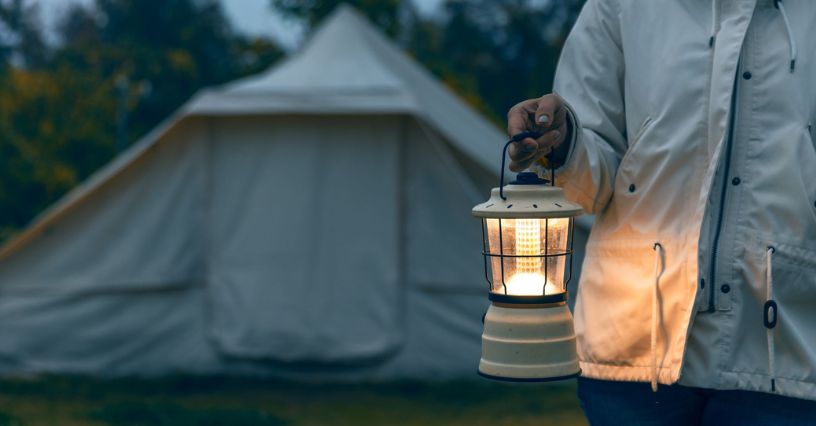Kobieta trzyma lampkę turystyczną przed namiotem w plenerze