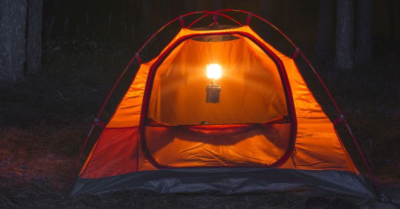 Lampka turystyczna oświetla wnętrze namiotu w lesie