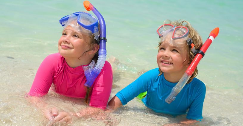 Dziewczynka i chłopiec w maskach do snorkelingu leżą na brzegu morza