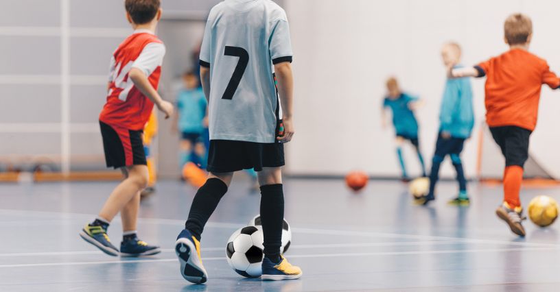 Dzieci w butach halowych grają w piłkę nożną na hali sportowej