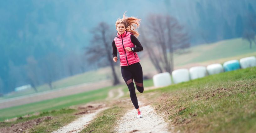 Biegaczka w bezrękawniku biegnie po wiejskiej drodze w chłodny dzień