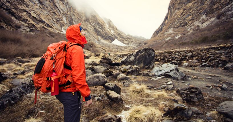 Mężczyzna w kurtce przeciwdeszczowej wędruje po górskim szlaku