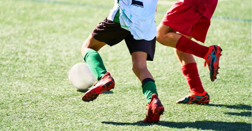 Dwóch młodych piłkarzy w korkach rywalizuje o piłkę na boisku